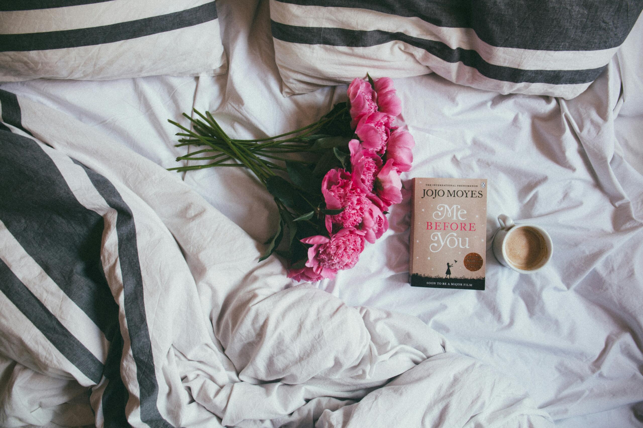 A flat lay of a double bed with flowers, a book and a cup of coffee. 