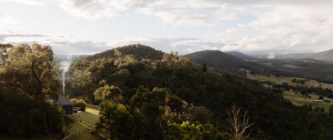 In the bottom left corner a sole a mud brick cabin is perched a long a bush range. A plume of smoke is coming out of its chimney evoking wintery vibes overlook the farms in the below valley. 