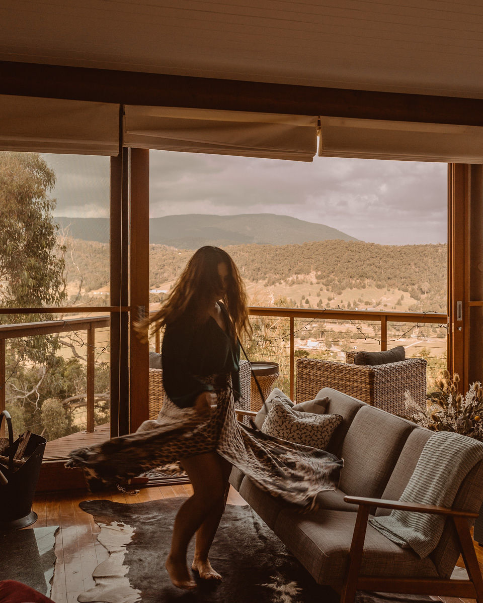 A women dancing on her own in a lounge room with a view of mountains in the background