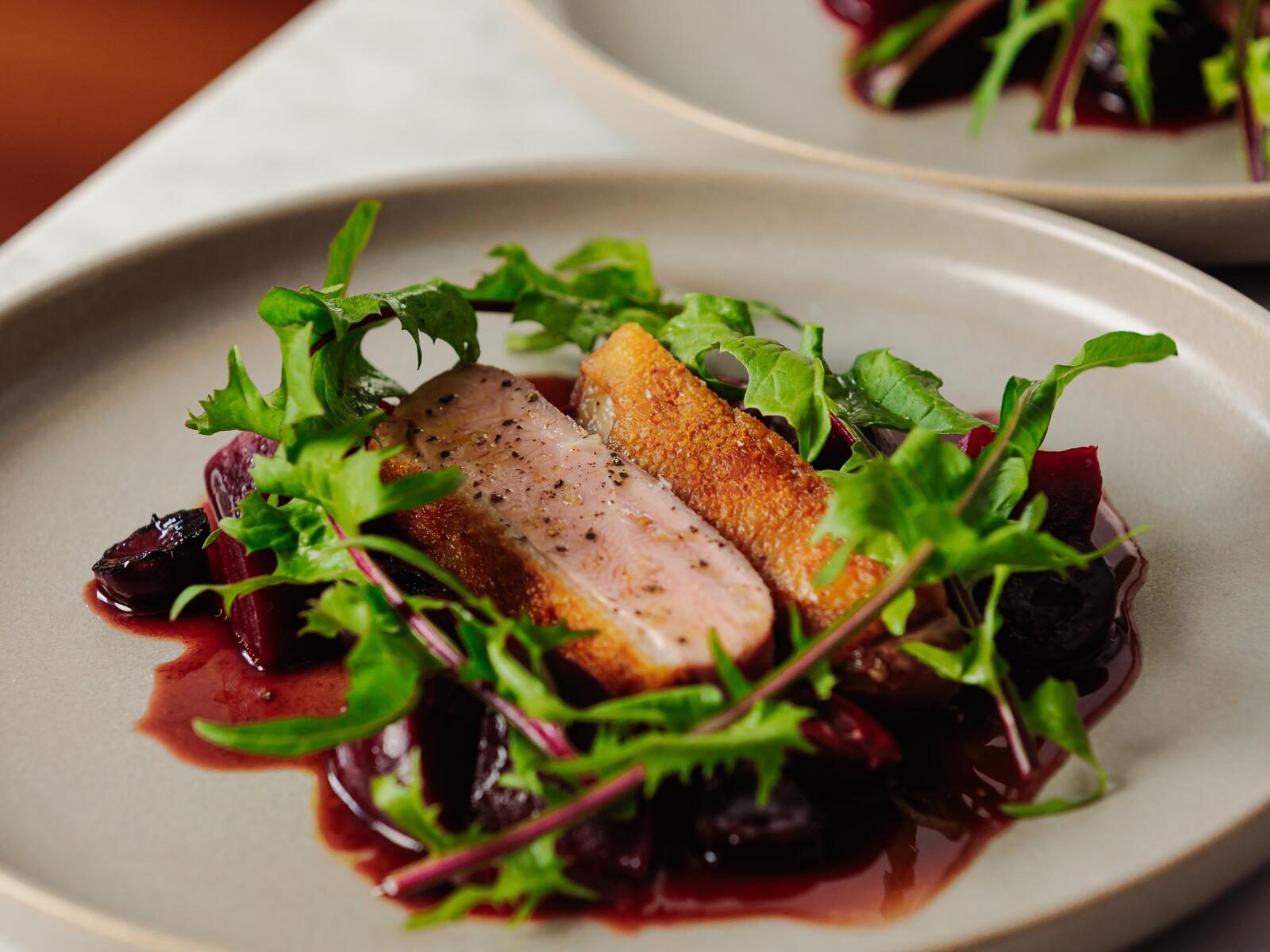 A restaurant plate with seasonal menu of duck with cherry.