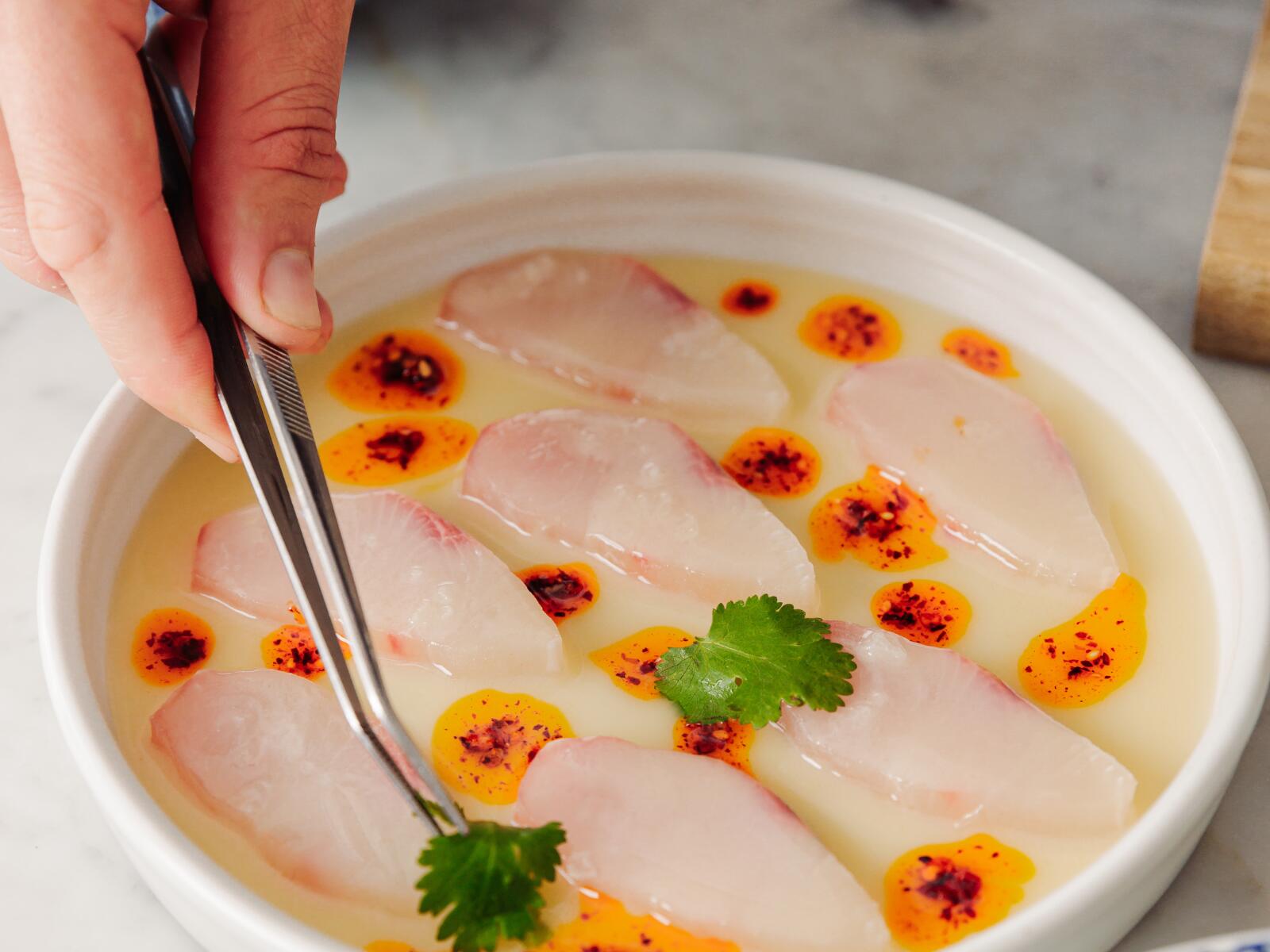 A chef preparing a dish with kingfish and fresh herbs